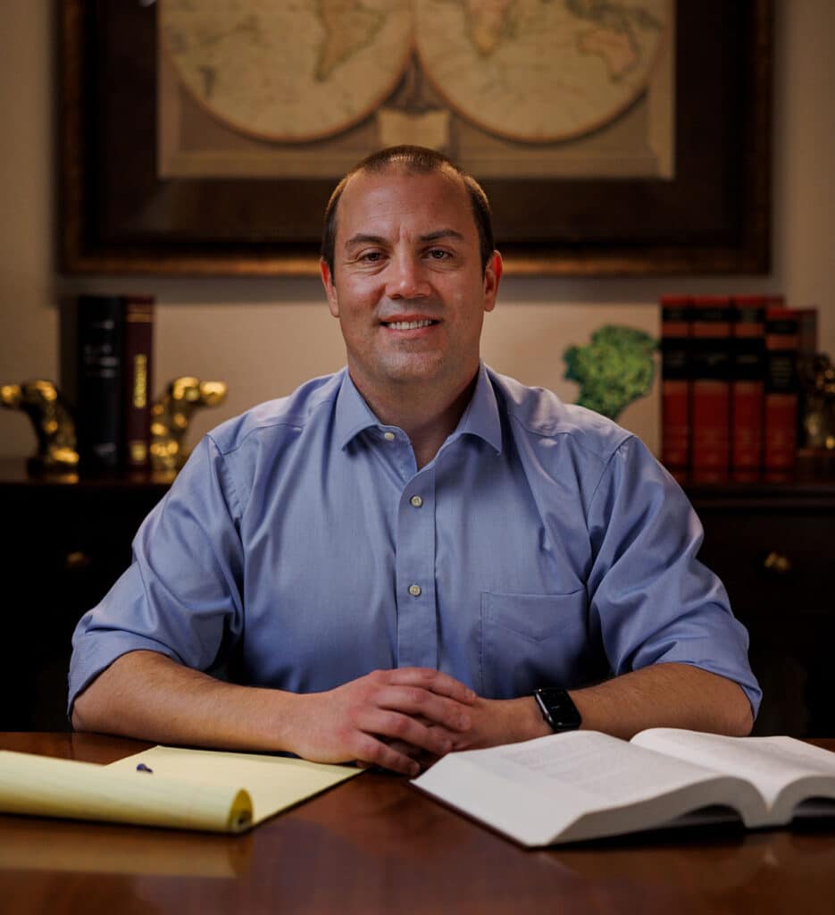 Attorney Michael McKeon in his Montana office, smiling and approachable, with a yellow legal pad and open book on his desk.