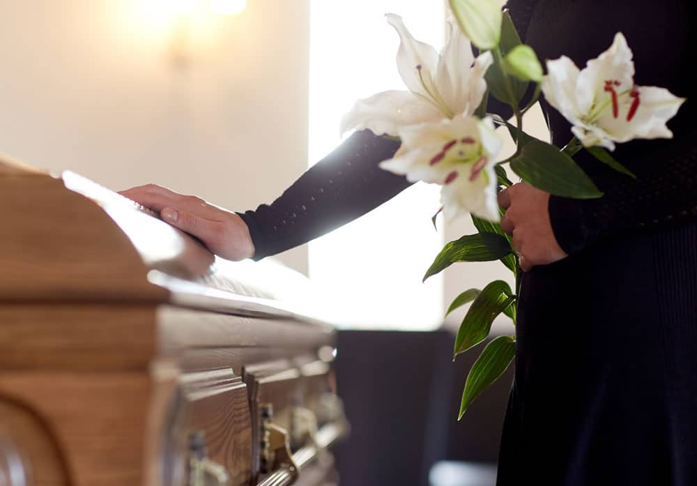 Mourner with flowers touching a casket – representing wrongful death legal support in Montana.
